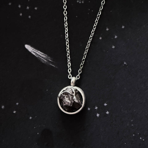 A beautiful and unique small round chunky raw meteorite necklace in a silver tone deep bezel. The perfect space-themed necklace jewelry gift!