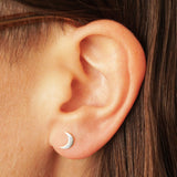 A cute mismatched pair of sterling silver moon and star stud earrings - the perfect space jewelry gift for a space lover! Showing the moon earring on an ear.
