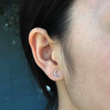 A pair of small sterling silver crescent moon stud earrings - the perfect space or moon jewelry gift for a space or moon lover! Shown on a woman's ear.