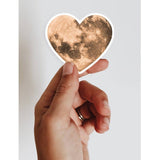 Hand holding a vinyl heart moon sticker, perfect for any lover of the moon or space!