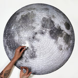 moon surface puzzle from Four Point Puzzles with 1000 pc round design. A space gift for space enthusiasts! Shows someone building the puzzle.